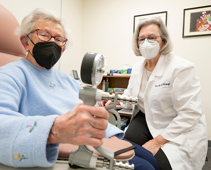 A person in a blue sweater holds a device while a doctor in a white coat looks on