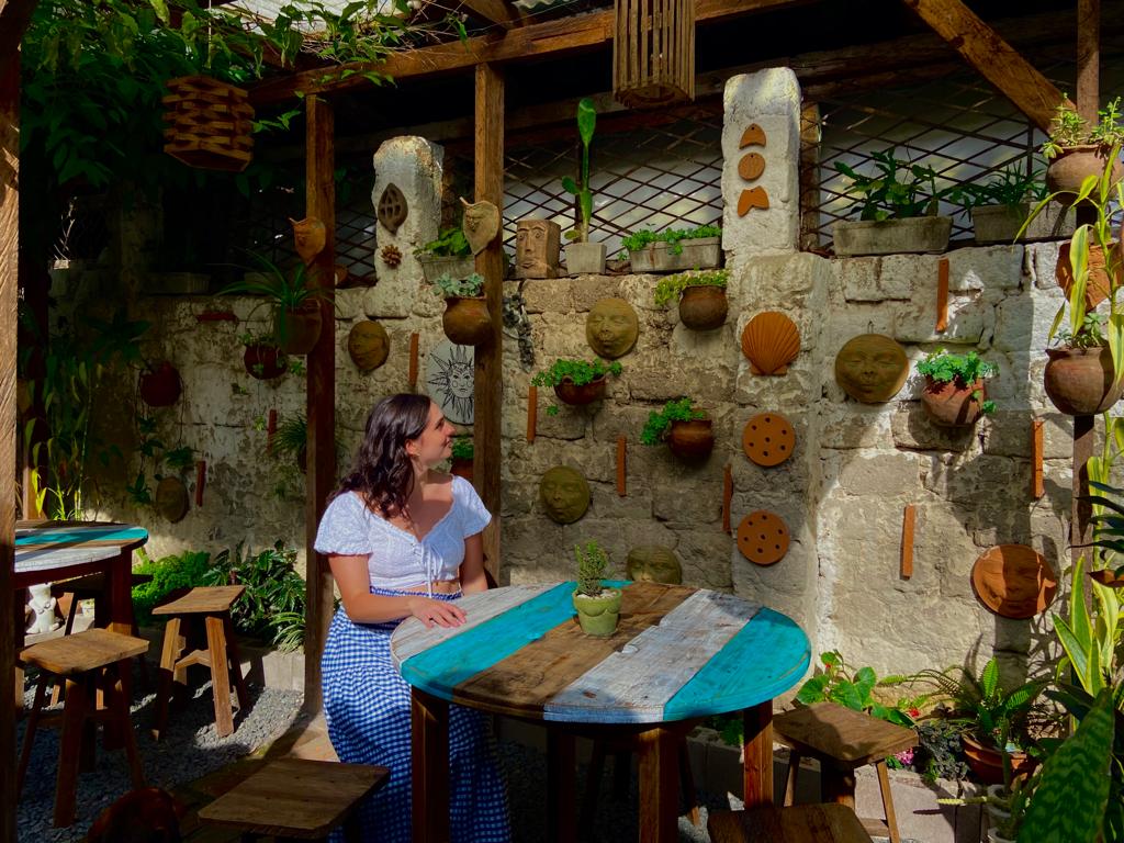 Adams sits at a wooden table looking at clay pieces on a brick wall