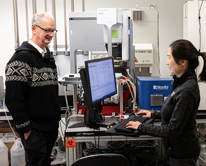 A person works at a computer while another stands behind the monitor