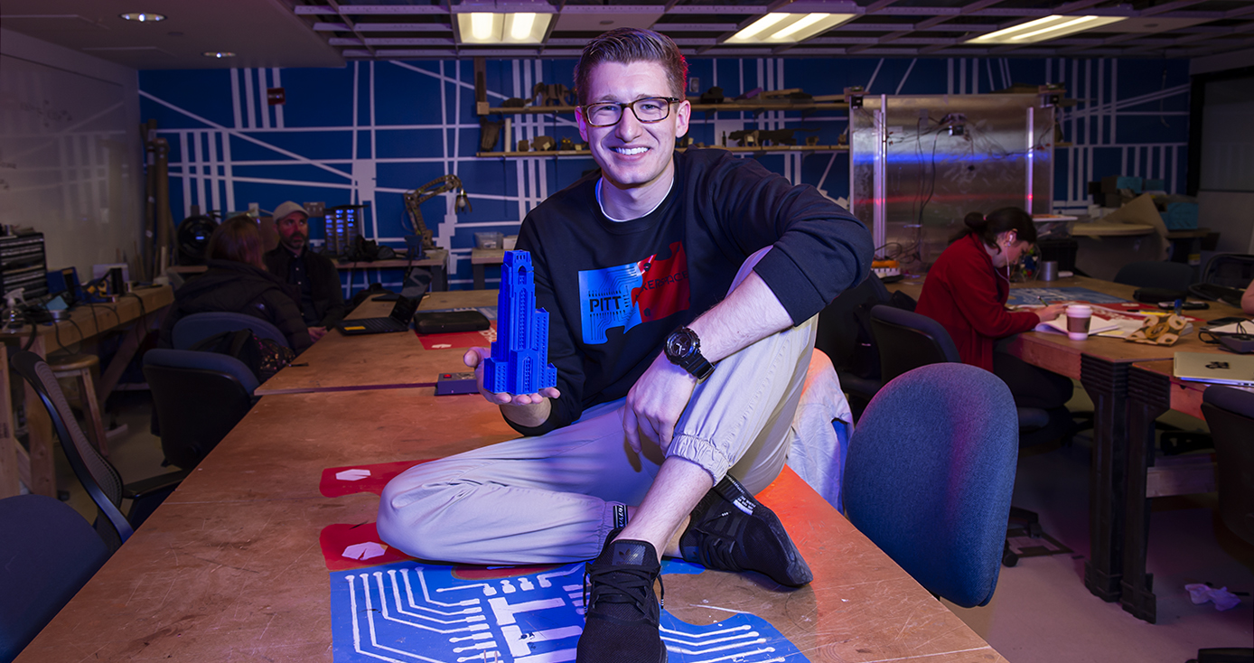 O'Brien sitting on a table in the Makerspace, holding a 3-D printed Cathedral of Learning