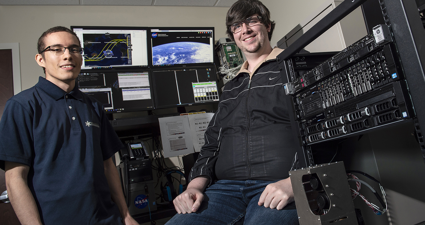 two men standing in front of a bunch of monitors and computer equipment