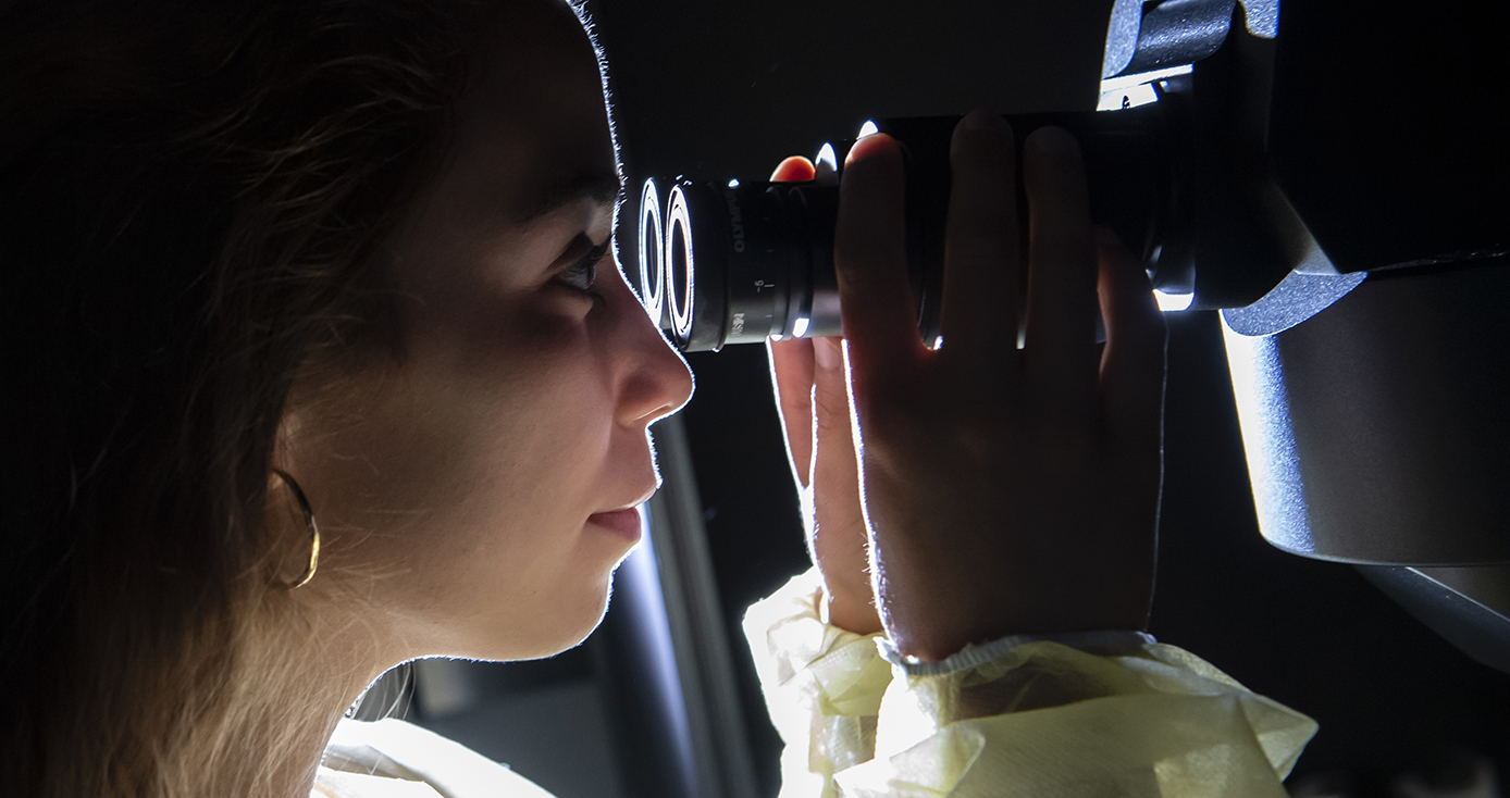 A person in gold earrings and a yellow top looks through an eyepiece