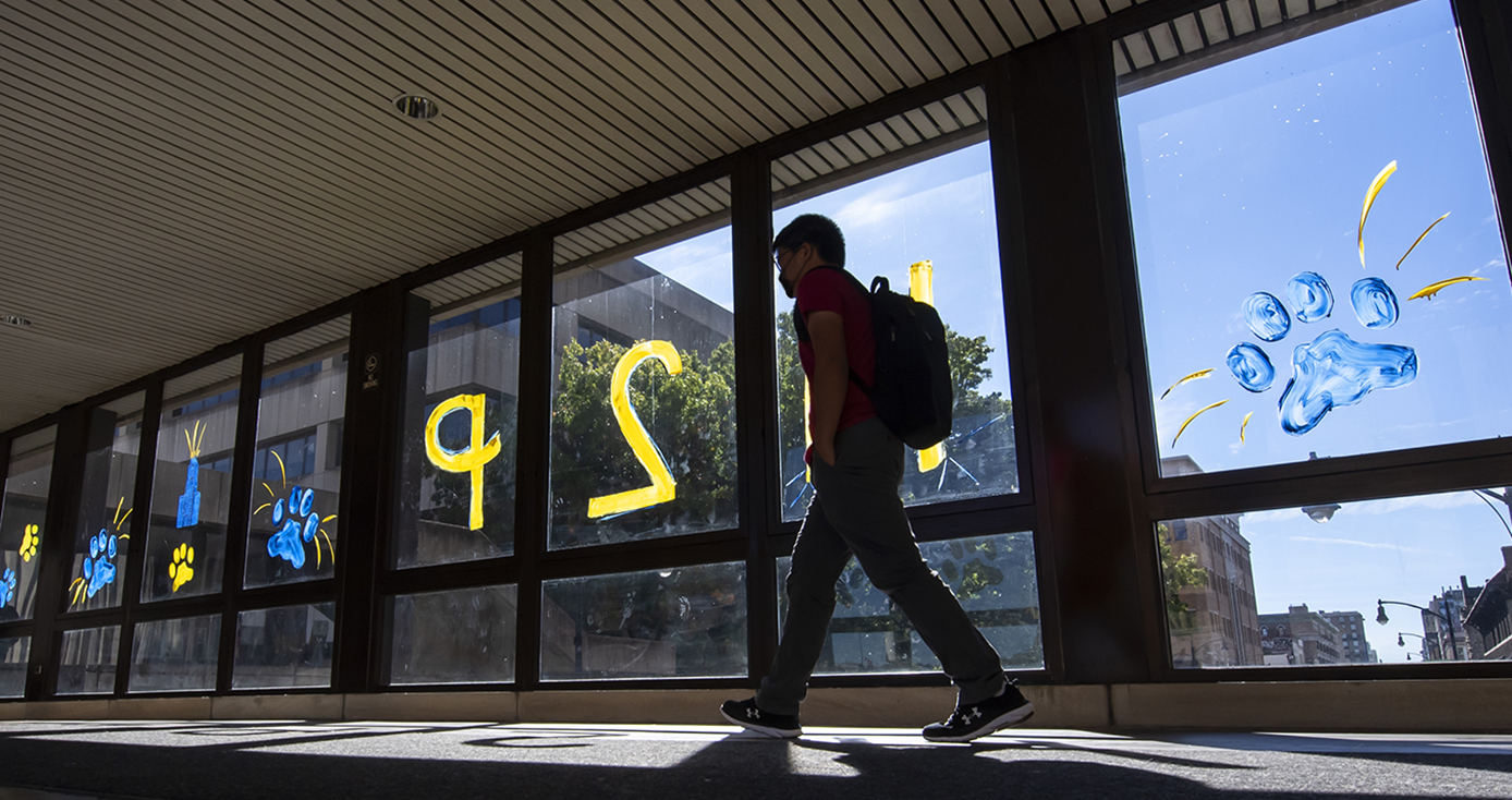 A person with a backpack walks in front of windows