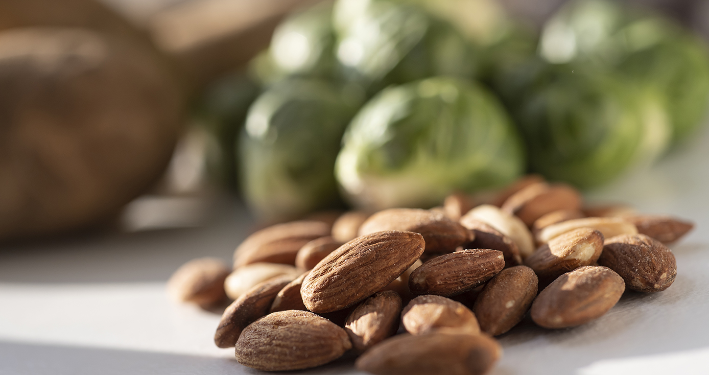 A pile of almonds in the foreground with Brussels sprouts behind them