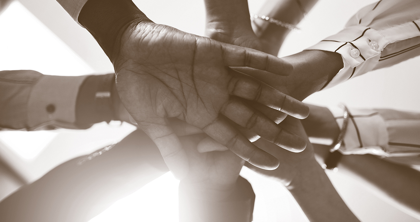 A sepia-tone photograph of 10 hands stacked on top of one another