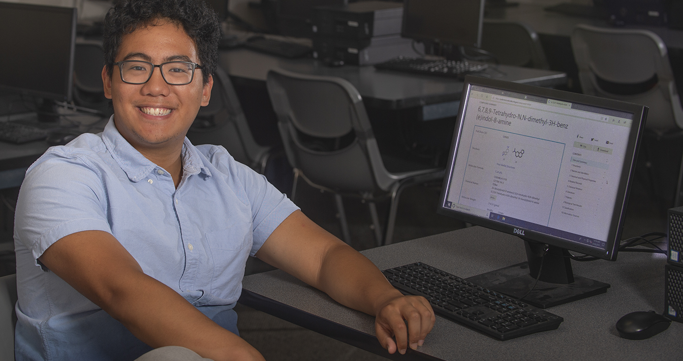 Joseph Valdecanas sitting at a desk in a classroom, showcasing a website that he helped create.