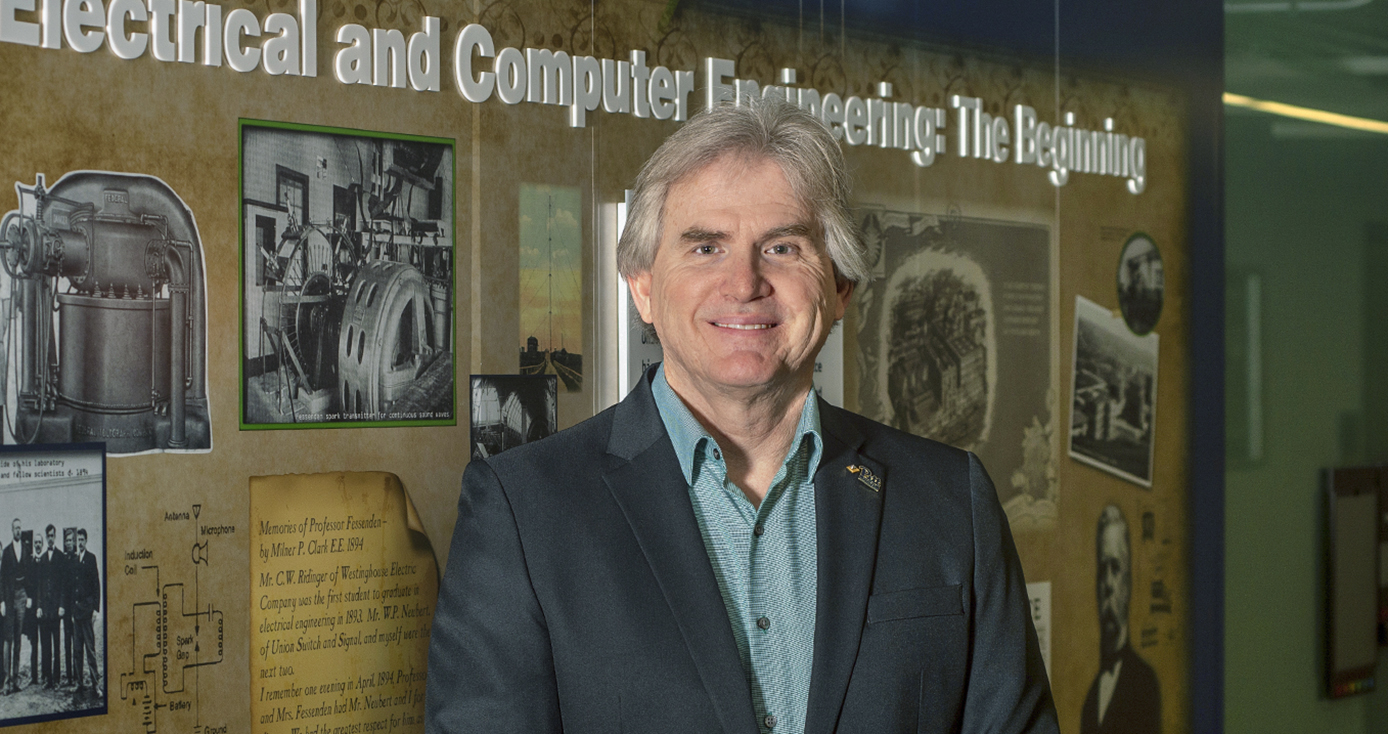 Alan George stands in a dark blue jacket and dress shirt. 