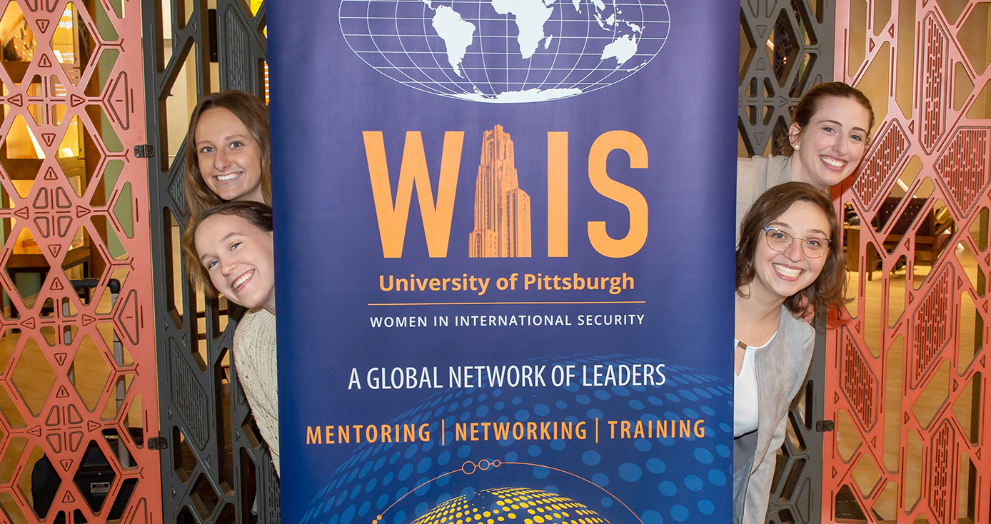 Four women pose next to a banner for Women in International Security