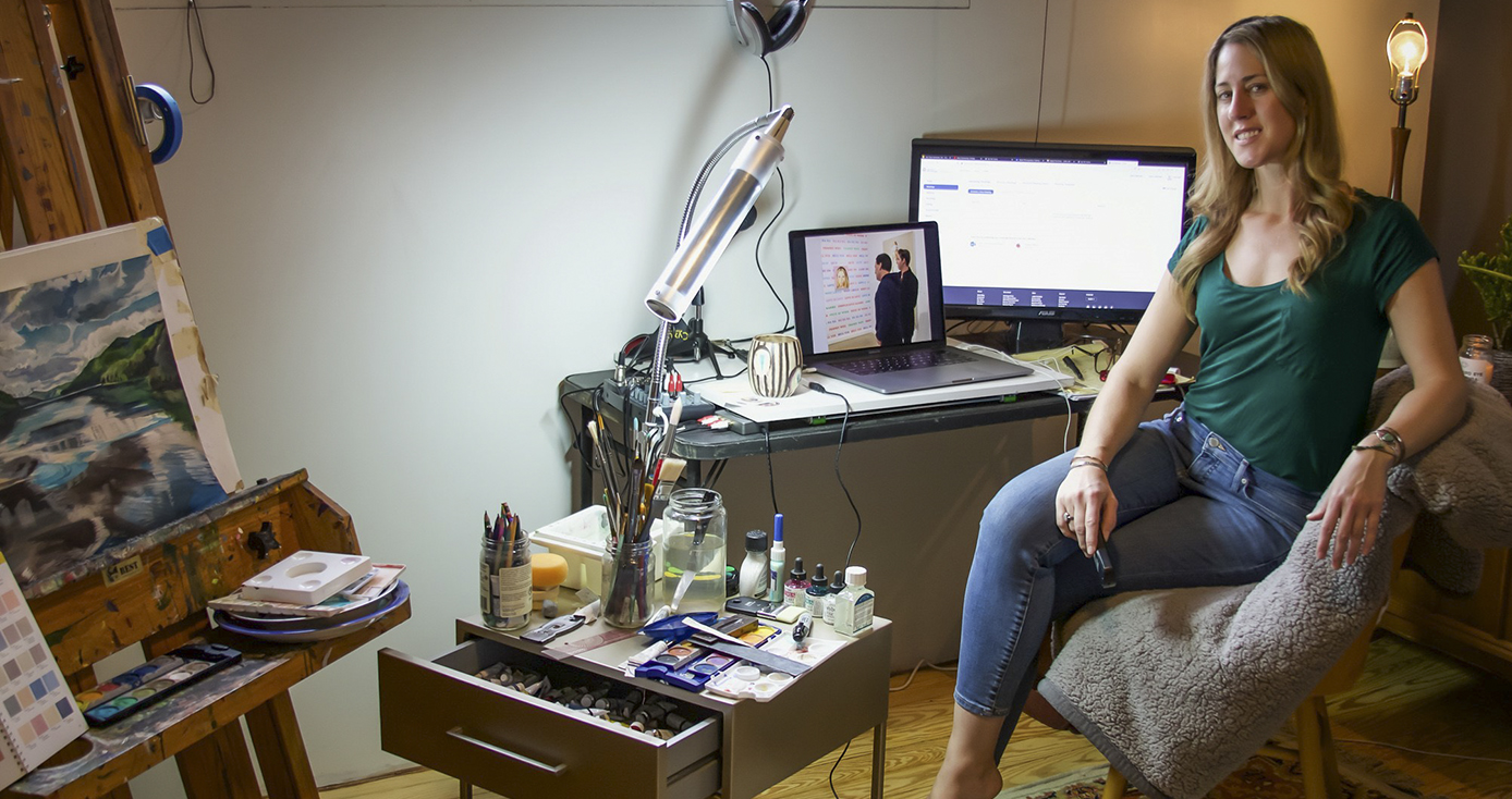 Anna Lemnitzer in front of her computer and a table of art supplies