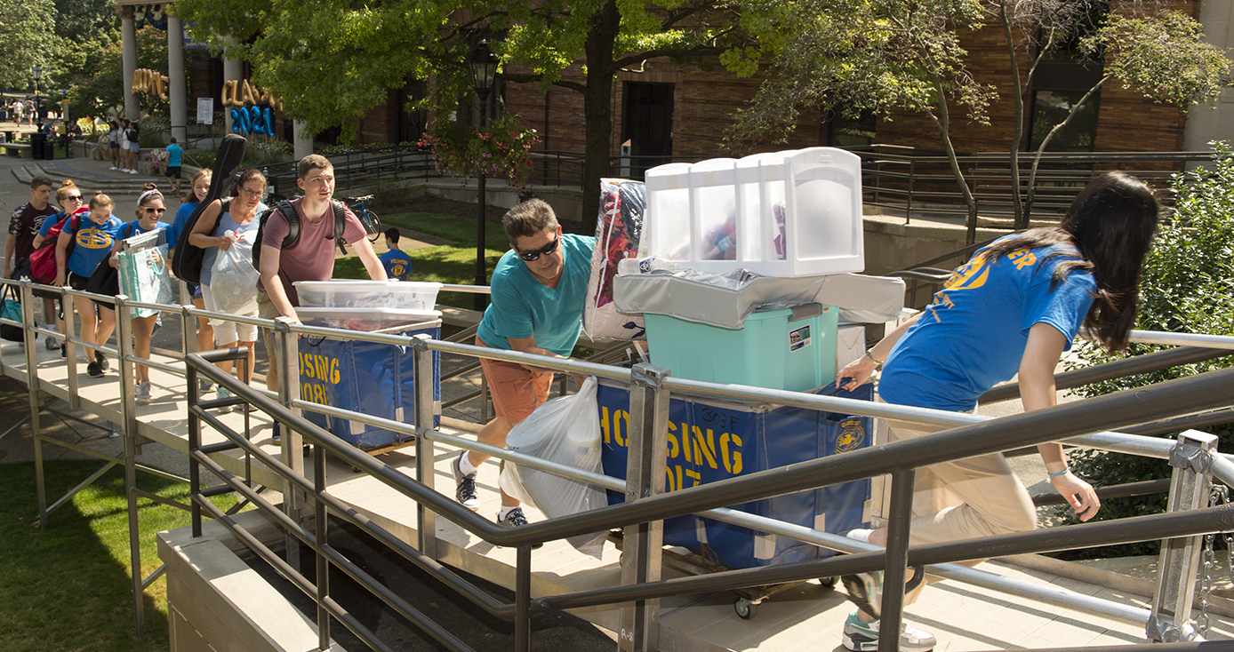 Several students pushing carts of belongings up a ramp