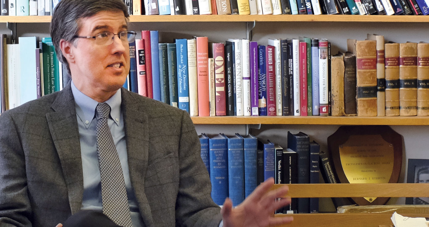 gray-haired Hibbitts with glasses sitting in front of a large bookshelf