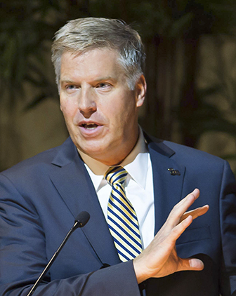 Chancellor Gallagher in a blue suit and blue and gold striped tie at a podium