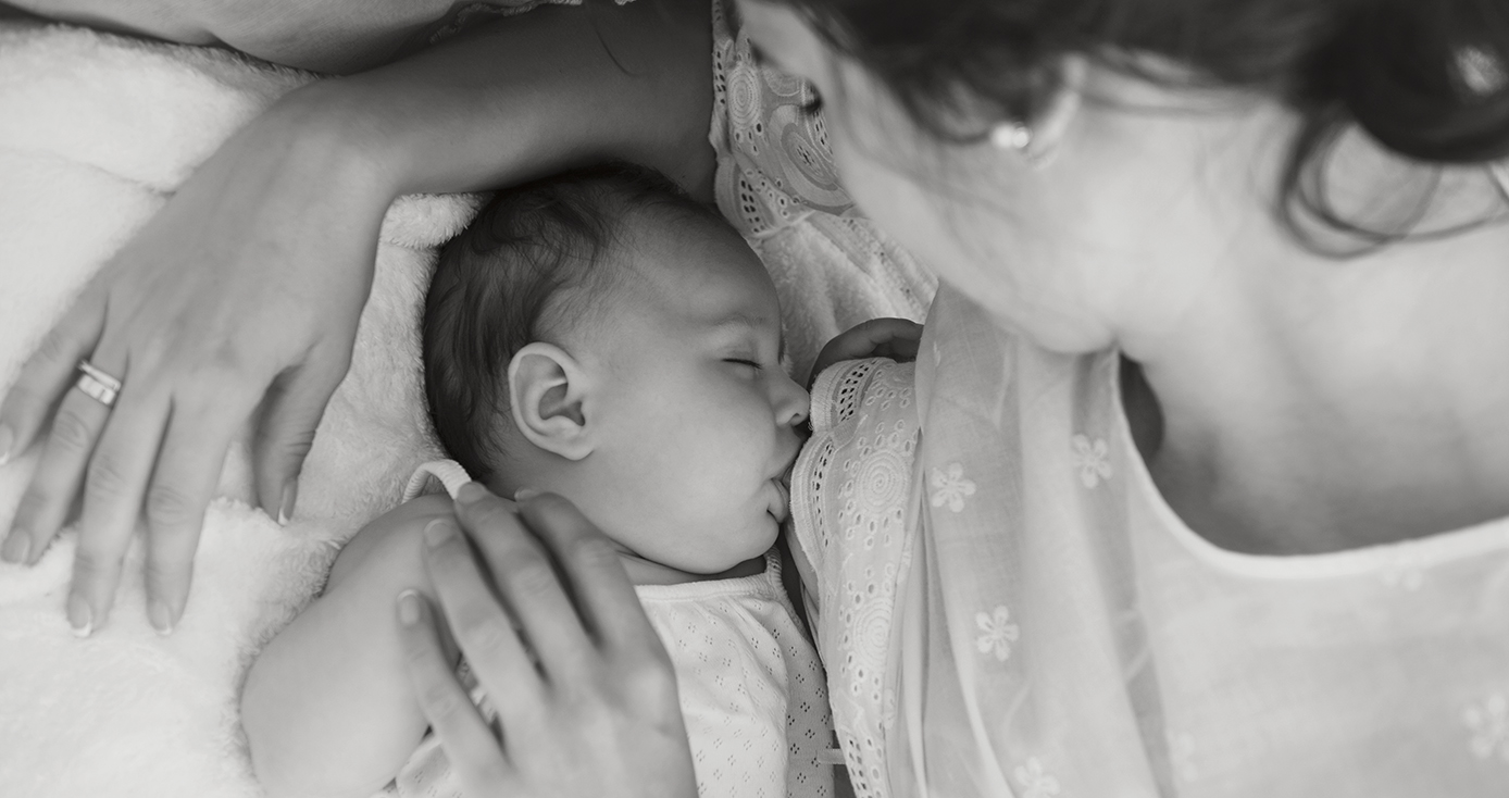 a black and white image of a baby feeding with their mom