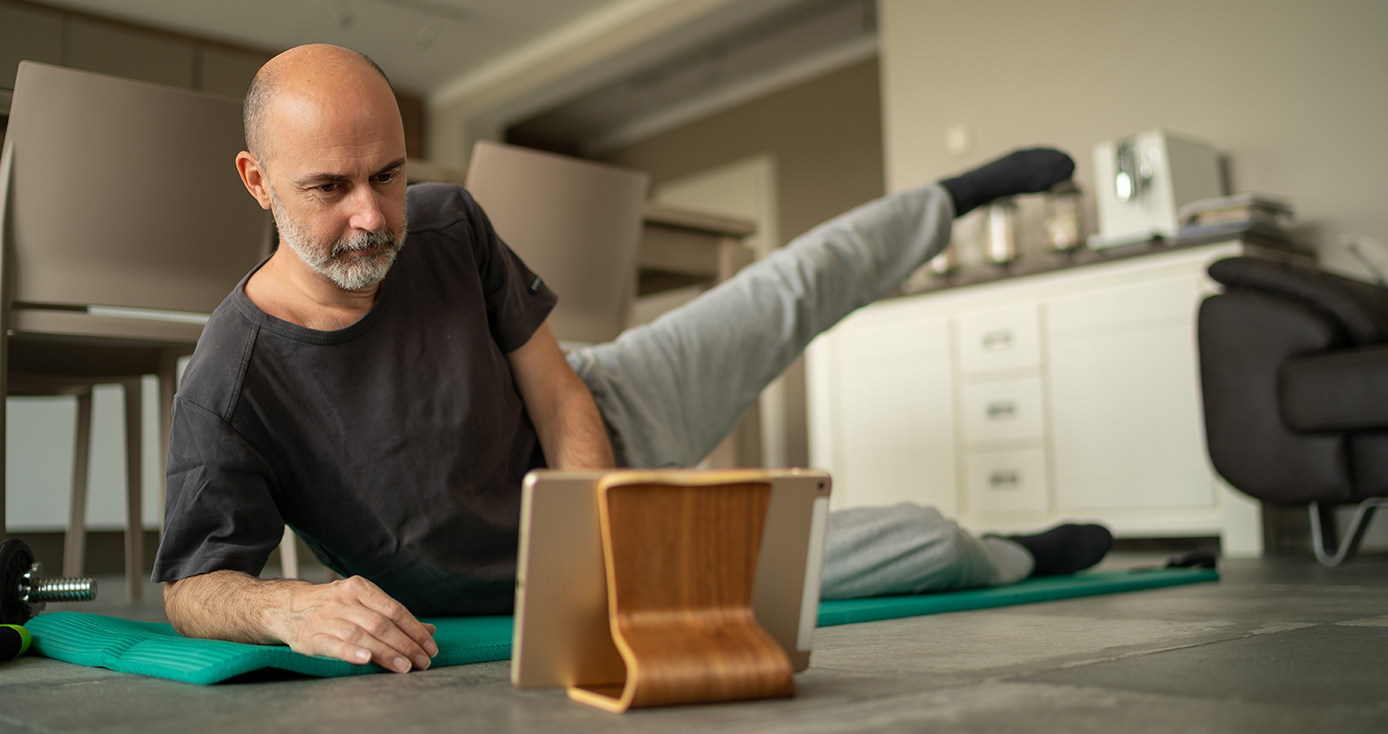 a man in a gray shirt and sweatpants exercises while watching a video on a tablet