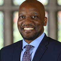 Bonner in a navy suit, light blue shirt and blue/red tie