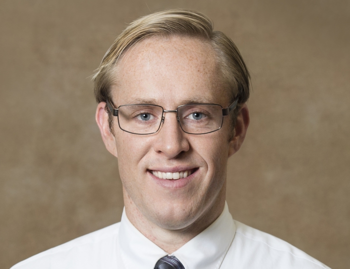 Lynch, a man with blond hair and glasses, in front of a tan background