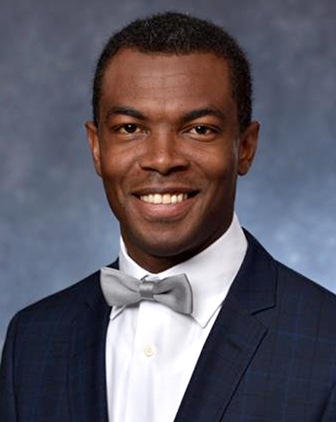 A man in a black suit, white shirt and silver bow tie