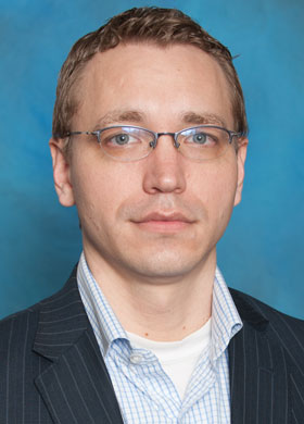 John R. Shaffer in a blue dress shirt and a suit jacket with a blue background