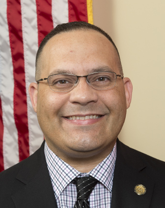 Hernandez in a suit and tie in front of the American flag