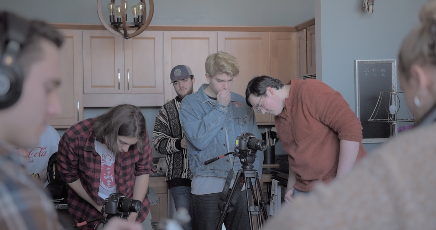 Students stand around a camera on a set