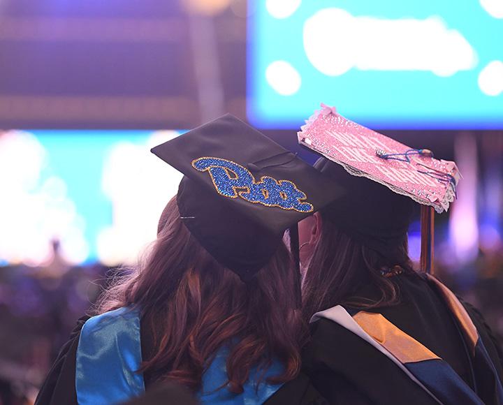 Two graduating seniors look up at a large arena screen