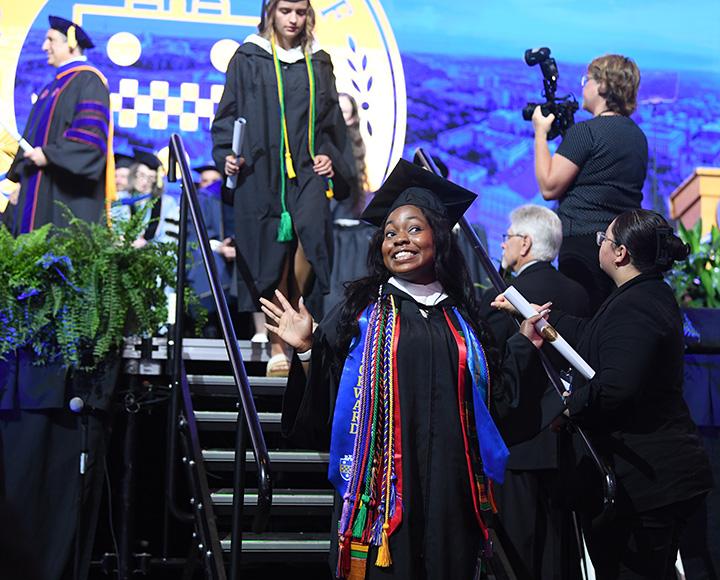 Student waving at the crowd with diploma in hand