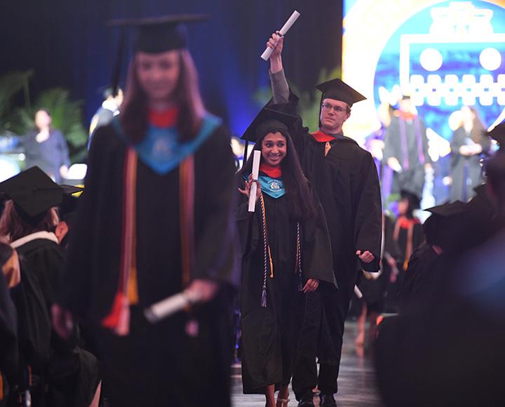 Several students walk down the aisle, diplomas in hand