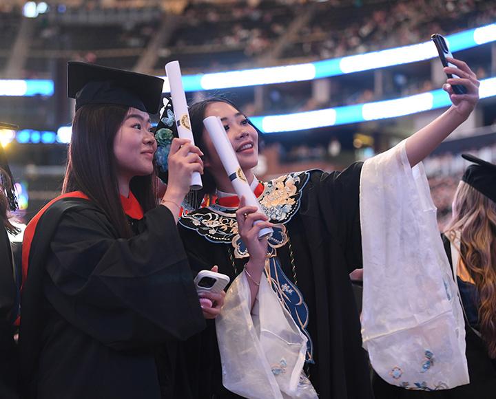 Two students take selfies with their diplomas