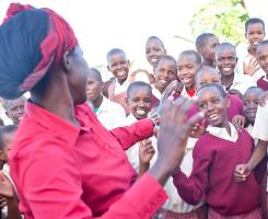 Children in red school outfits dance with a woman in a red collared shirt