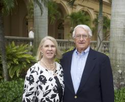 Woman and man in dressy attire pose in front of palm trees.