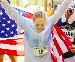 Frederick holds her arms up in front of an American flag after finishing Badwater