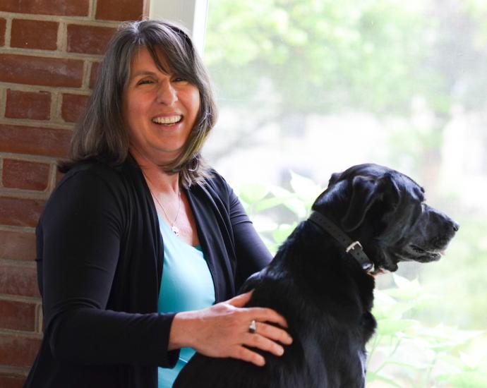 A woman smiles while petting her dog.