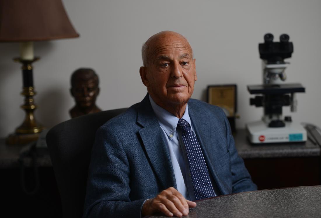 Man in suit sits behind desk.