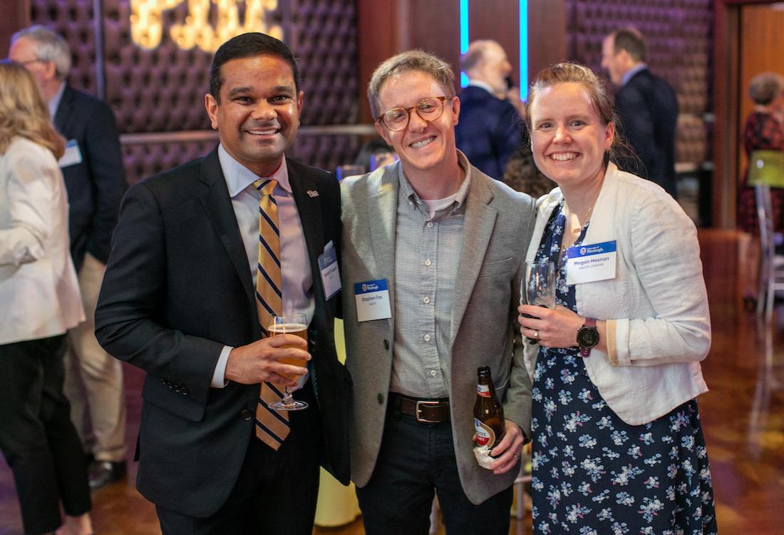 Three people hold drinks and smile for camera.