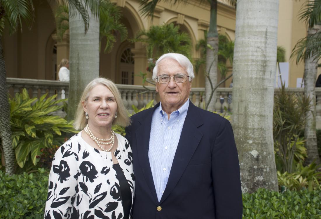 Woman and man in dressy attire stand in front of palm trees.