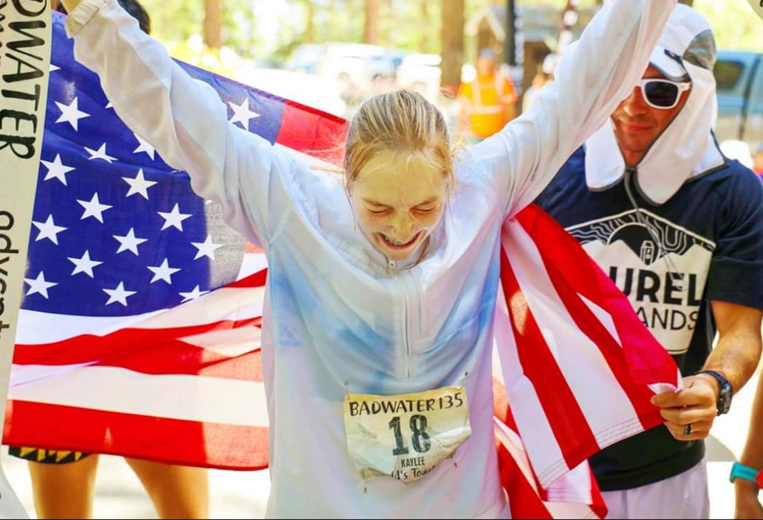 Frederick holds up her arms in front of an American flag after finishing Badwater