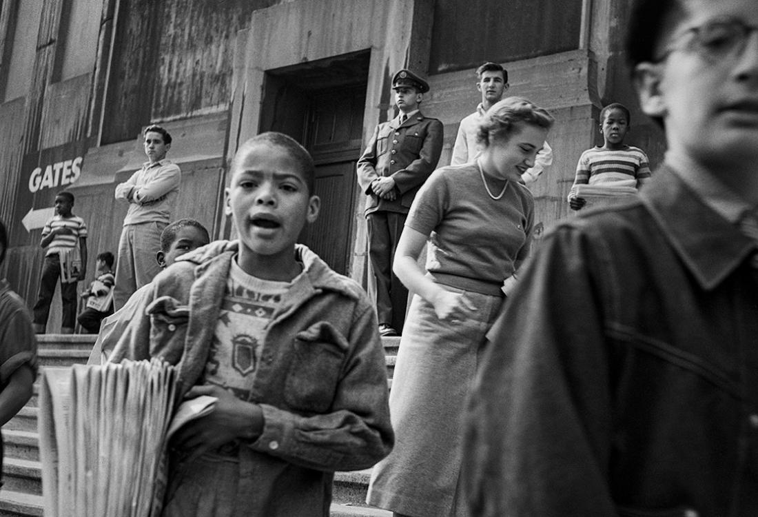 A black and white photo of a paperboy shouting in front of a crowd on steps