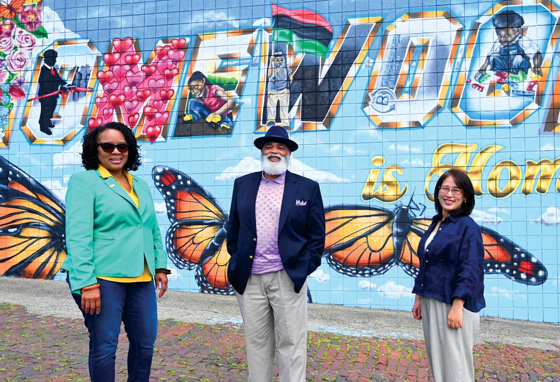 Two women and one man stand in front of a colorful mural.