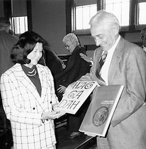 A person in a suit hands books to Bruhns