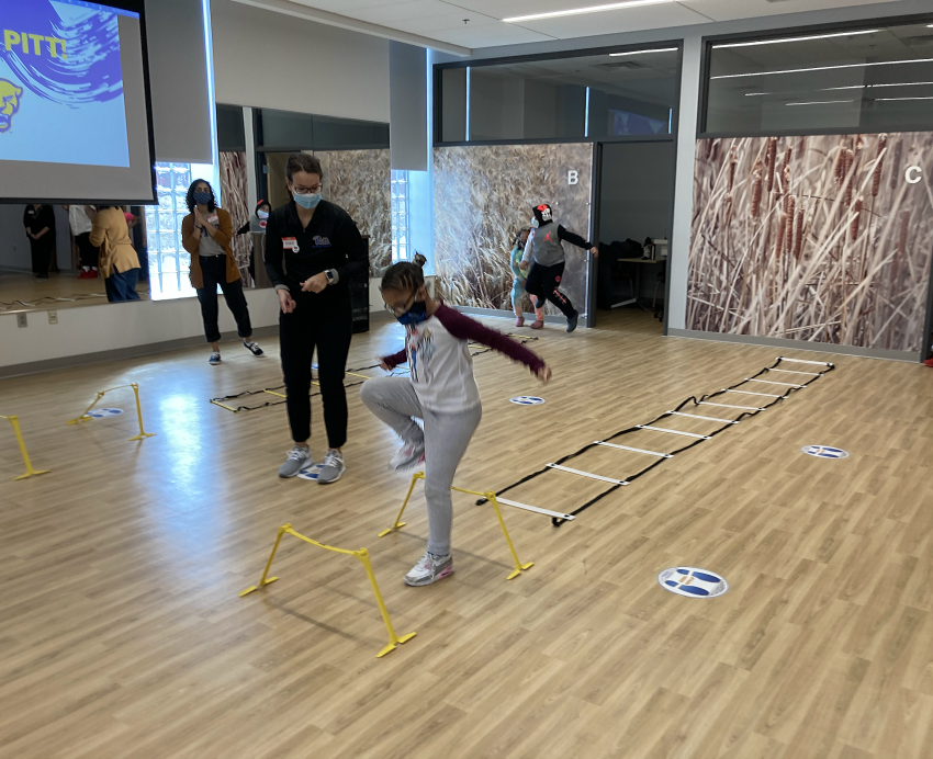 children and adults in a gym jumping over a rope ladder on the ground