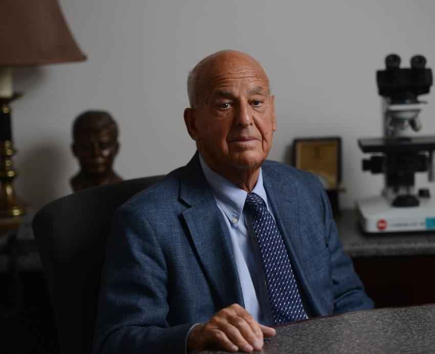 A man in a suit sits behind a desk.