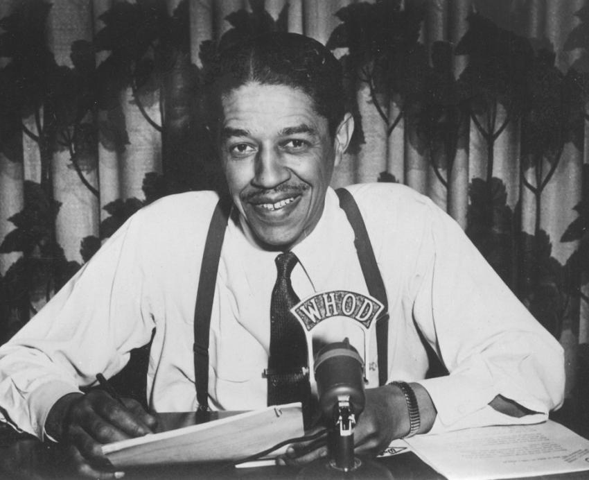 Man sitting at desk behind a microphone.