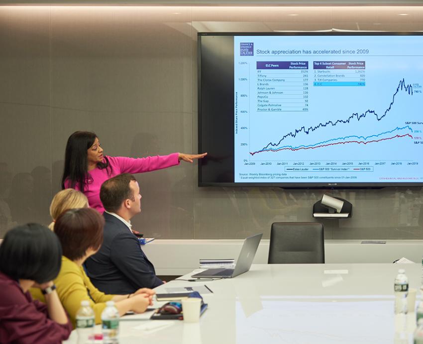 Woman gives presentation in boardroom, pointing to chart showing business growth